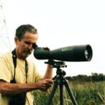 A telescope set up on a sturdy tripod with an observer adjusting the eyepiece.