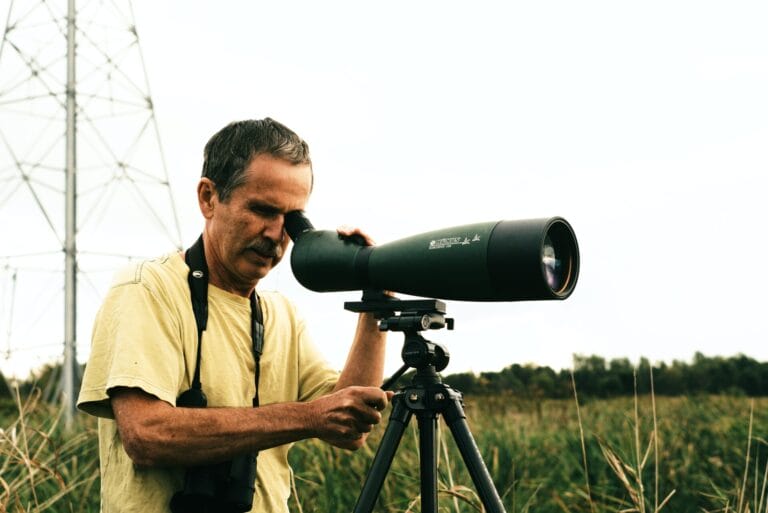 A telescope set up on a sturdy tripod with an observer adjusting the eyepiece.